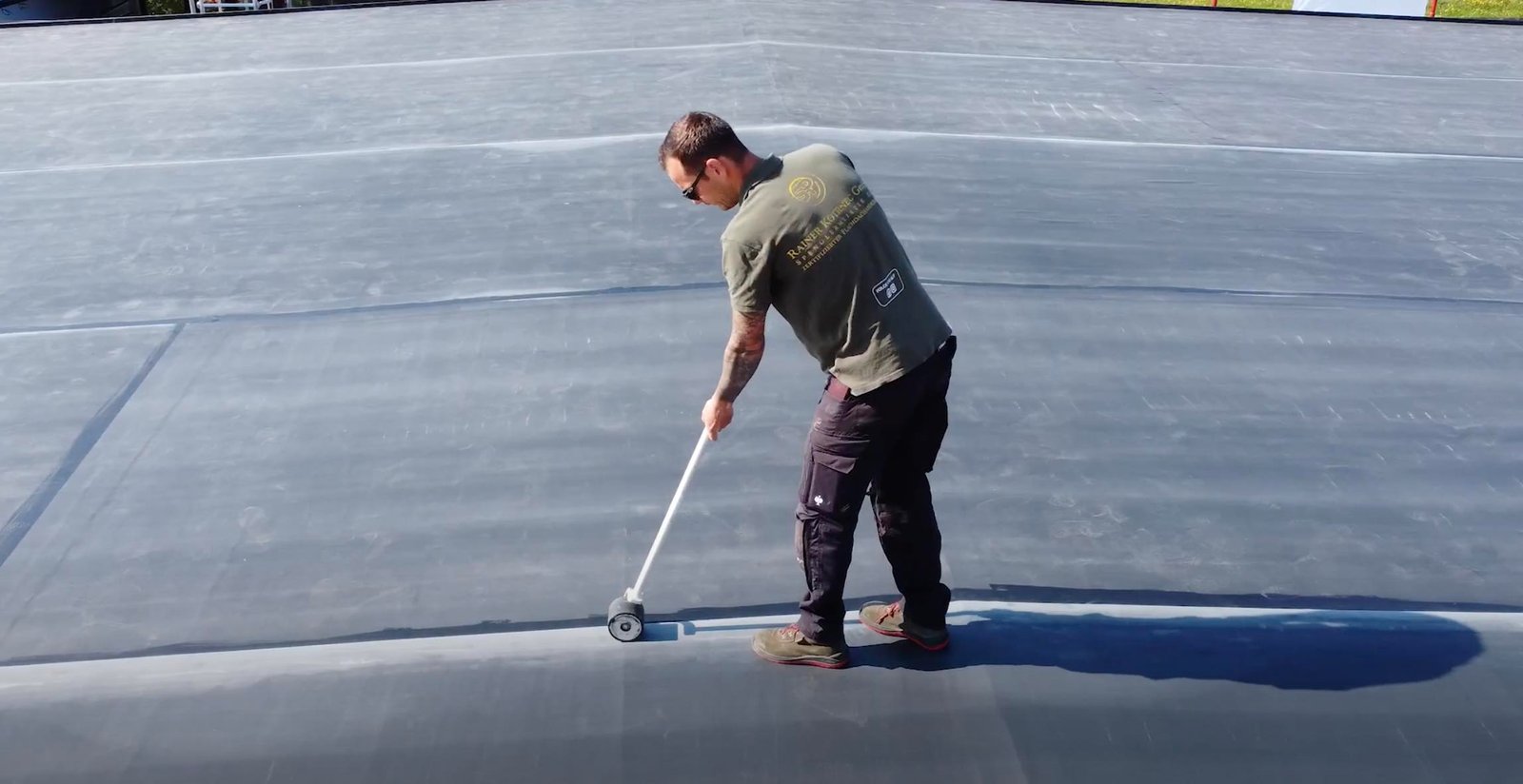 A worker applying liquid waterproofing on a roof using a brush.