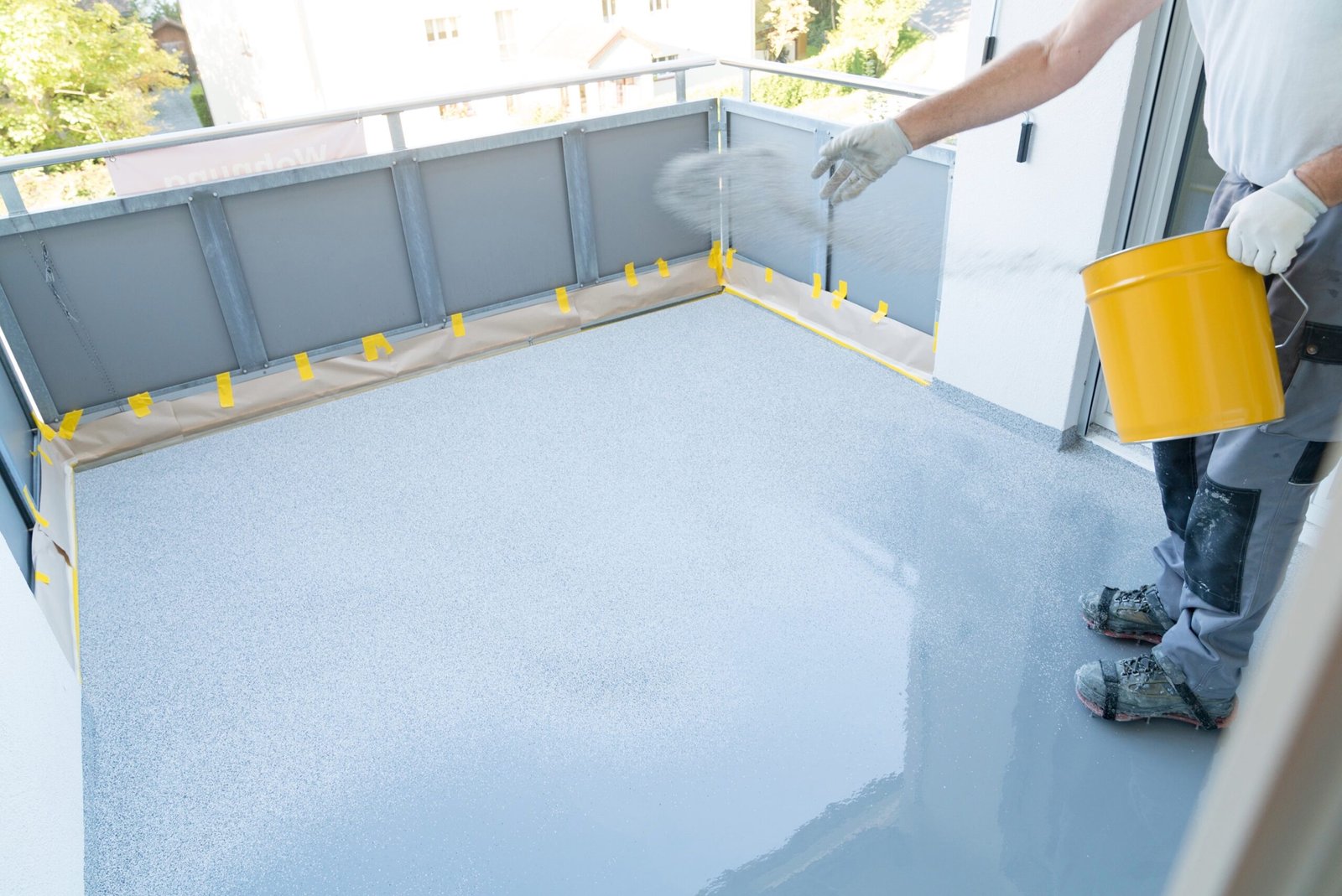 A man painting a concrete floor with a bucket, applying liquid waterproofing.