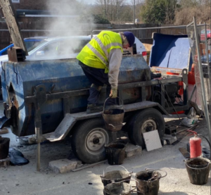  A worker is seen applying Mastic Asphalt Waterproofing to a large blue truck, enhancing its waterproof capabilities.