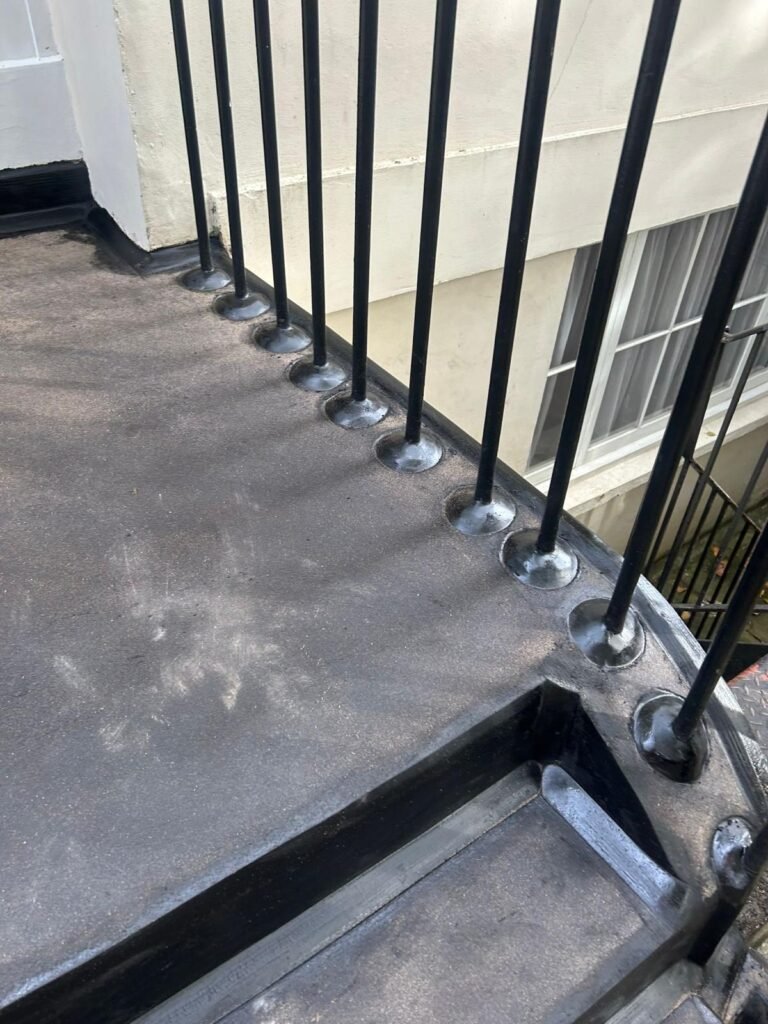 A picture of a black asphalt staircase with a smooth surface and neat edges, leading down from a small landing with black metal railings.