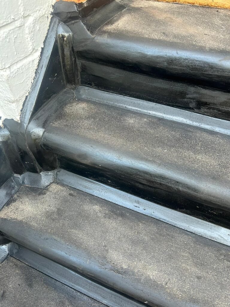 A close-up of black asphalt steps with smooth edges, showing a neat finish where the steps meet the white wall, looking strong and clean