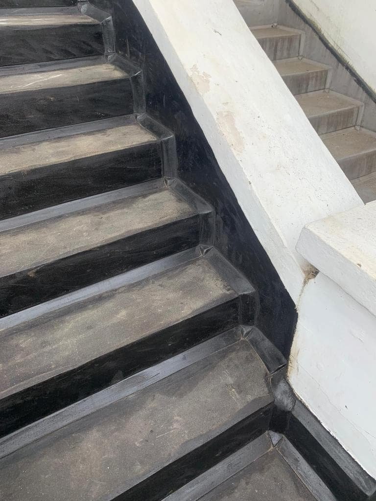 Close-up image of repaired steps with black mastic asphalt applied on the surface and edges, showing the smooth texture and defined corners of the step edges.