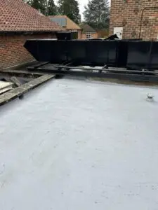 A flat roof featuring a large black tank, showcasing signs of an old applied liquid coating.