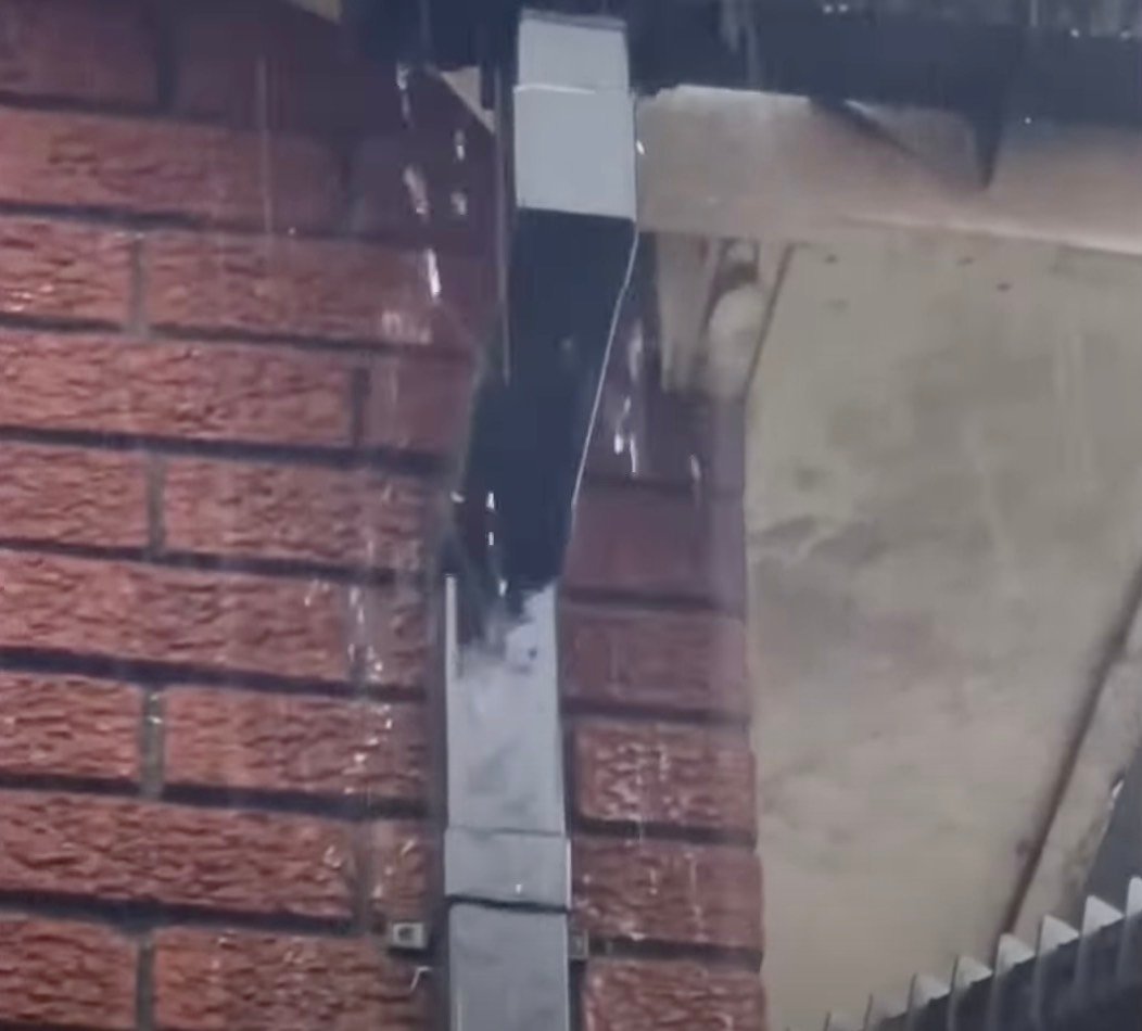 Leaking gutter with rainwater dripping down a brick wall.