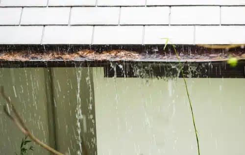 Overflowing gutter with water cascading down, showcasing a common issue during heavy rain, highlighting the need for gutter maintenance.