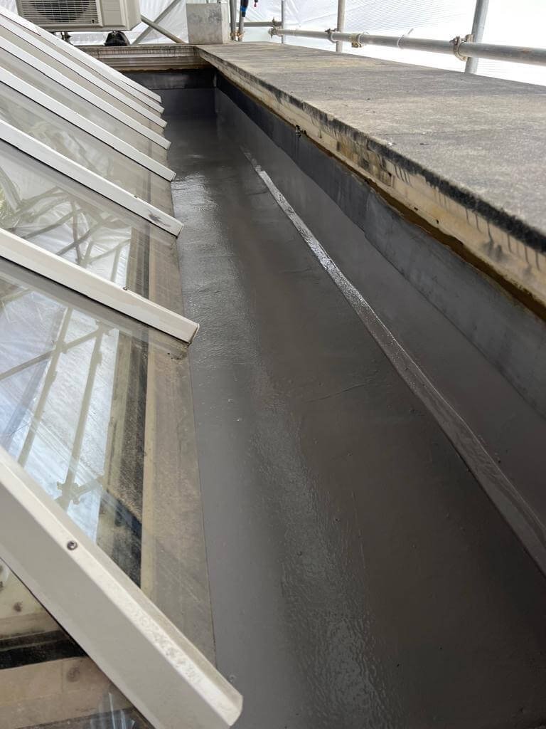 Freshly applied asphalt damp proofing on roof valley beside skylight windows
